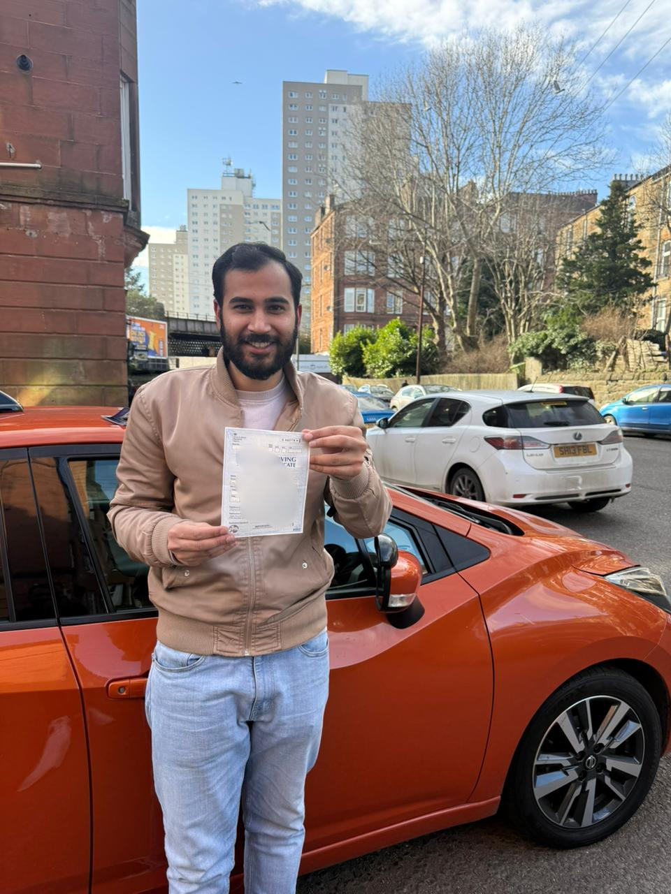 happy student holding driving test pass certificate beside car after passing test in Glasgow